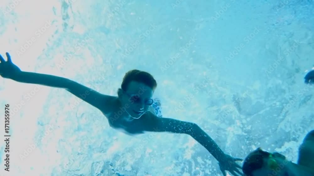 Boy swimming underwater in swimming pool with underwater camera POV