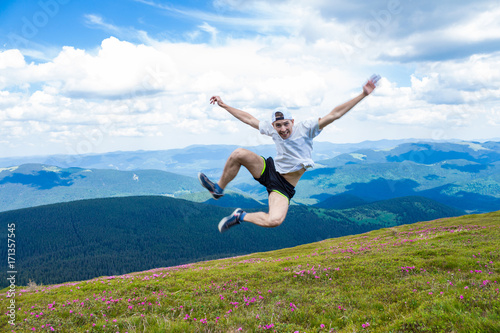 Happy handsome man tourist jump high into the sky for joy during the walk in beautiful mountains