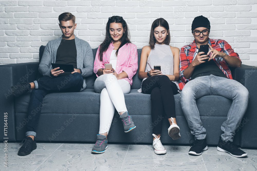 Young friends people looking down at cellular phone. Sitting on the couch and ignoring each others with on the smart phones. Young friends people looking down at cellular phone. Sitting on the couch and ignoring each others with on the smart phones.