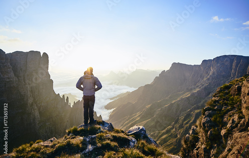 A Male hiker standing on a mountain edge admiring the spired mountain valley at sunrise.