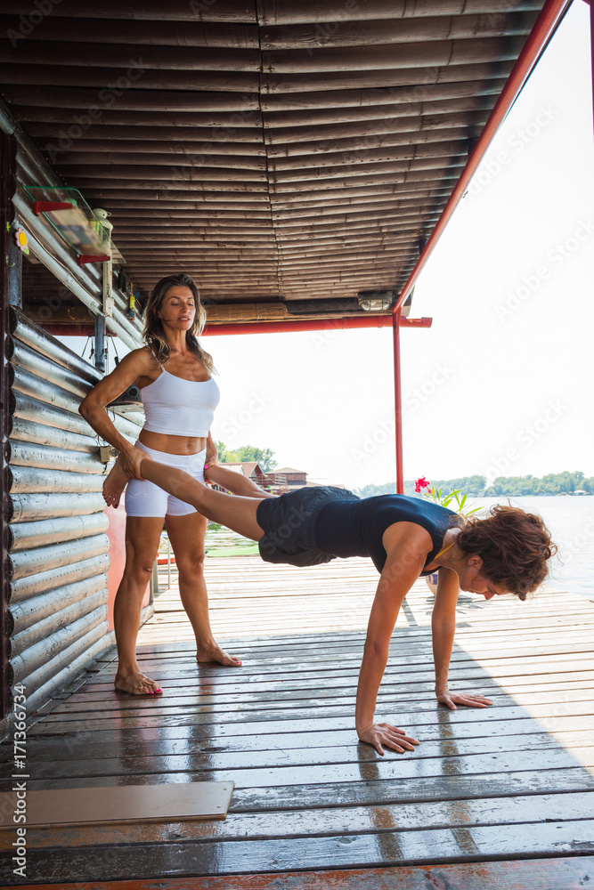 woman fitness instructor assisting young woman in exercise outdoor shot