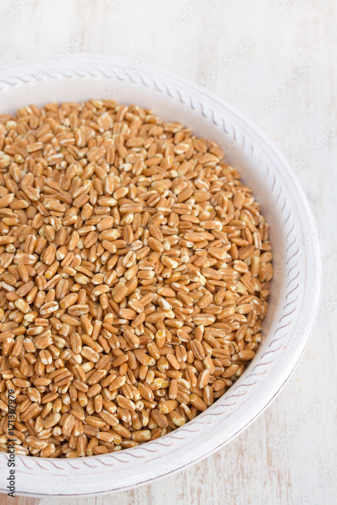 uncooked spelt on white plate on wooden background uncooked spelt on white plate on wooden background