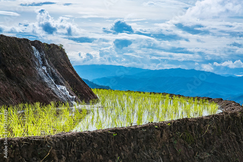 Water is flowing from a higer layer of rice terrace to a lower layer of rice terrace with mountains at the background in a cloudy light. photo