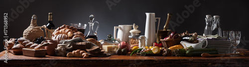 Rich food table, medieval style, panorama on rustic wood table and dark background.