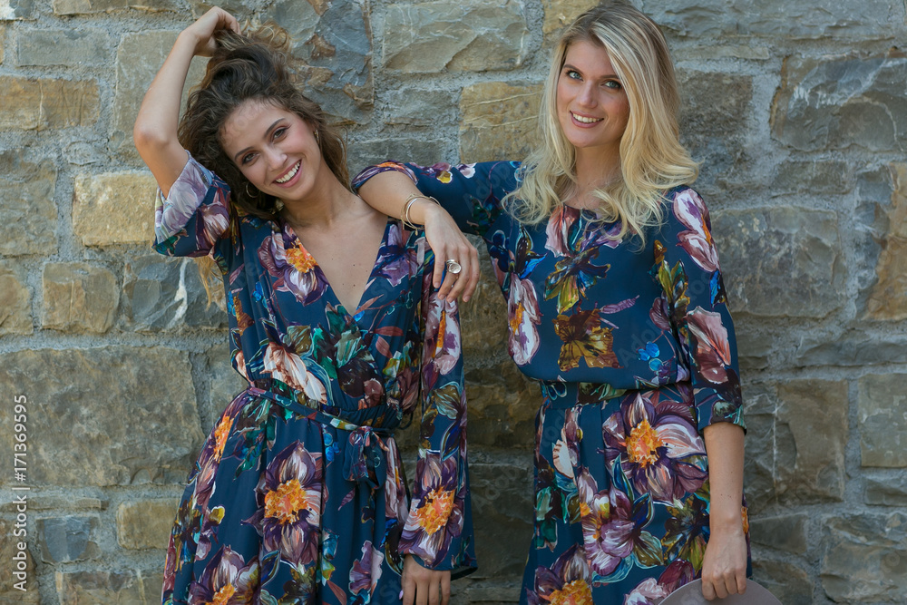 Fashion portrait of two happy woman with blue eyes in flower dress. Fashion hat in a sunny day. Girl with long blonde healthy hair and beautiful smile. Fashion portrait of two happy woman with blue eyes in flower dress. Fashion hat in a sunny day. Girl with long blonde healthy hair and beautiful smile.