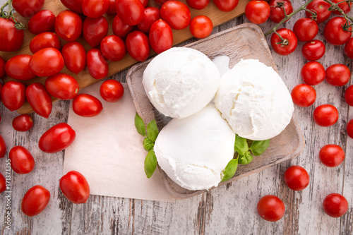 Tre mozzarelle intere di latte di bufala in un piatto di legno su un tavolo con pomodorini rossi