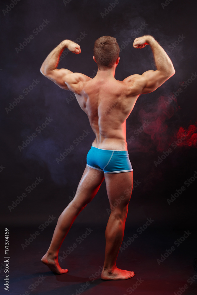 Young handsome muscular man bodybuilder with perfect abs, shoulders,biceps and triceps demonstrating huge muscles, full length portrait, view from the back Young handsome muscular man bodybuilder with perfect abs, shoulders,biceps and triceps demonstrating huge muscles, full length portrait, view from the back