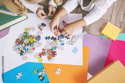 Two preschool age child put the puzzle together on the floor, hands close up
