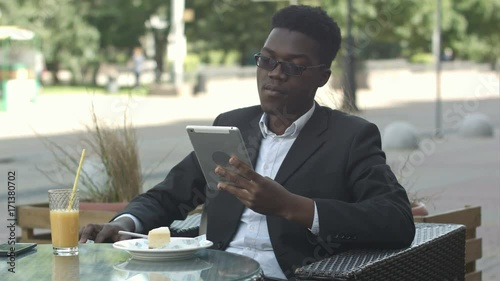 Handsome afro american man is using a tablet, while sitting in outside cafe photo