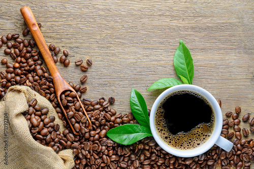 Obraz na plátně Coffee cup with beans, wood spoon, hemp sack bag and green leaf on wood table