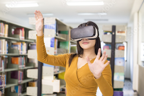 Woman in the foreground using VR for Seach information. Young Asian Woman using VR in the library. People with visual reality  concept.