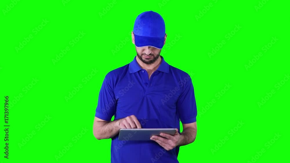 Caucasian delivery man working with a digital tablet while wearing blue uniform in front of green screen background Caucasian delivery man working with a digital tablet while wearing blue uniform in front of green screen background