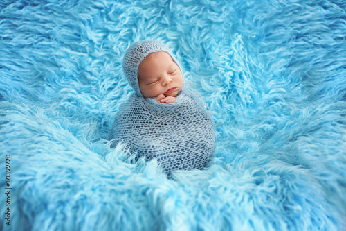 Cute baby boy, peacefully sleeping wrapped in brue wrap on a blue fur