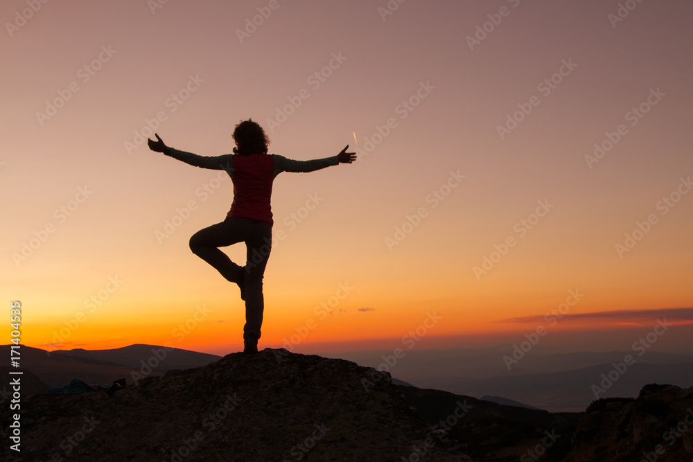 Silhouette of happy joyful young attractive woman playing yoga and having fun at the mountain against the sunset. Freedom, sport, adventure and leisure vacation concept.