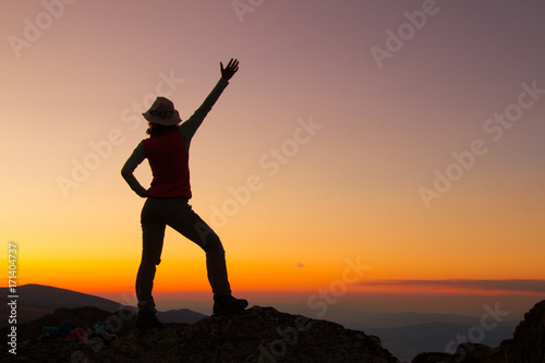 Sunset Silhouette of attractive woman staying and looking happy on top of the mountain. Freedom  adventure and leisure vacation concept.