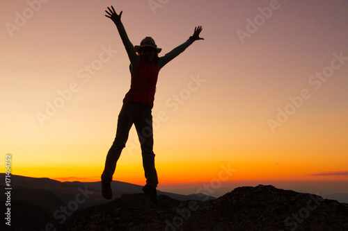 Silhouette of happy joyful young attractive woman jumping and having fun at the mountain against the sunset. Freedom  adventure and leisure vacation concept.
