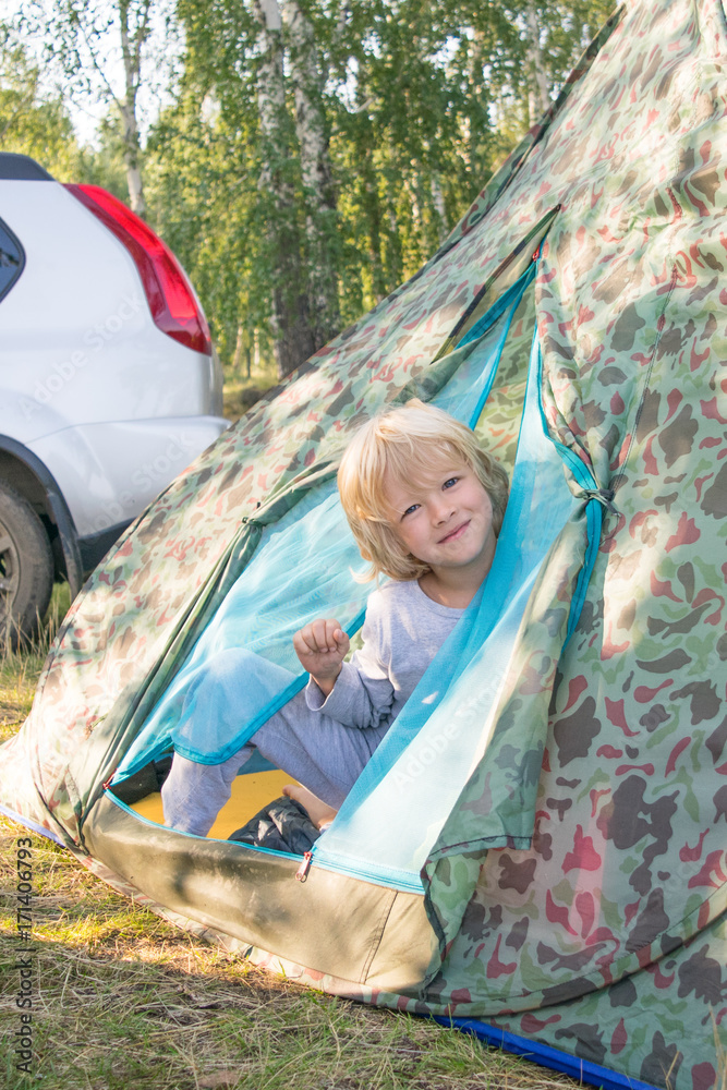 Sleepy blond boy gets out a tent in a morning