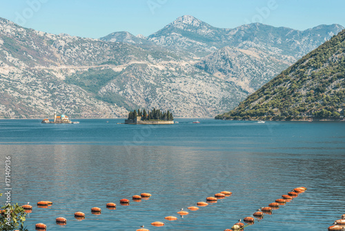 View of a fragment of an oyster farm on the background of the mountains and the island of Gospa with a small church and the island of Our Lady of the rocks with the same name church in Kotor Bay.
