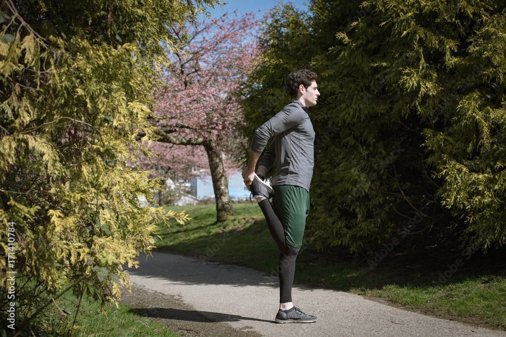 Side view of man doing stretching while standing on footpath at