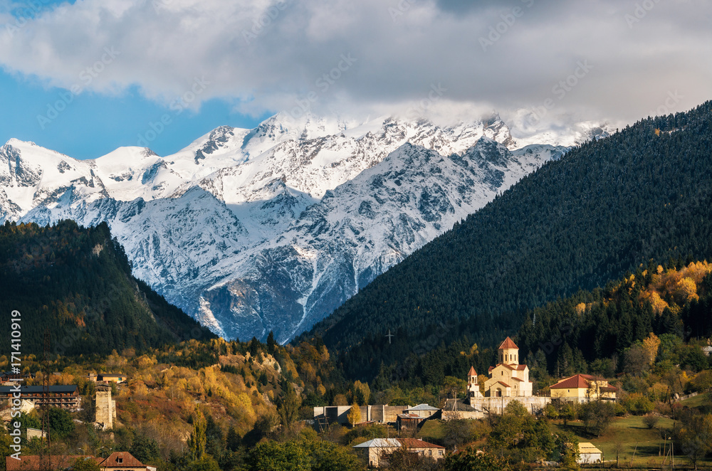 View of Svanetian towers and church in Mestia village against mountains with glaciers snow peaks. Upper Svaneti, Georgia. Georgian landmark