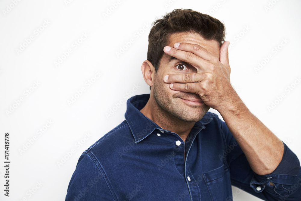 Guy in blue shirt peeking out from hand over eyes Guy in blue shirt peeking out from hand over eyes