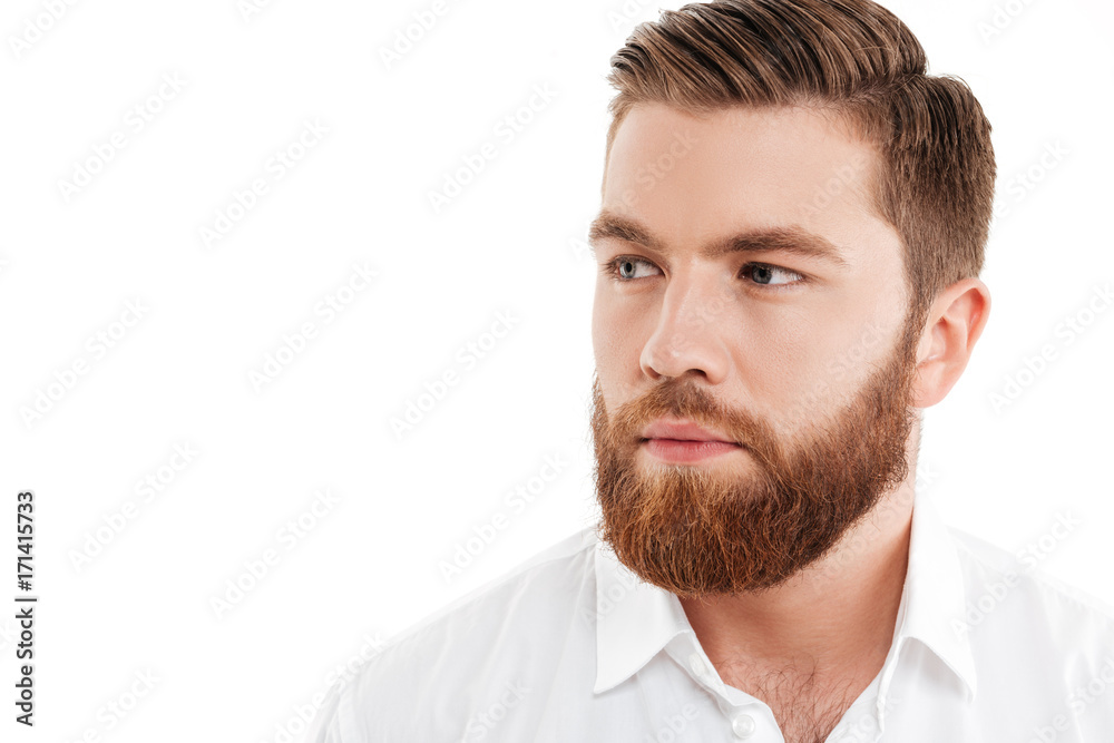 Obraz premium Serious young bearded man standing over white wall
