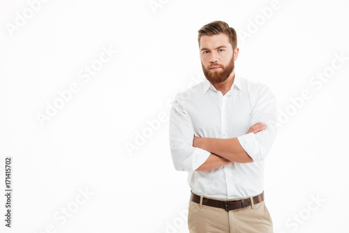 Serious young bearded man standing over white wall