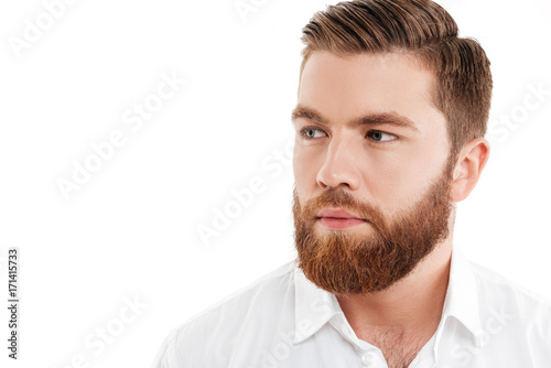 Serious young bearded man standing over white wall