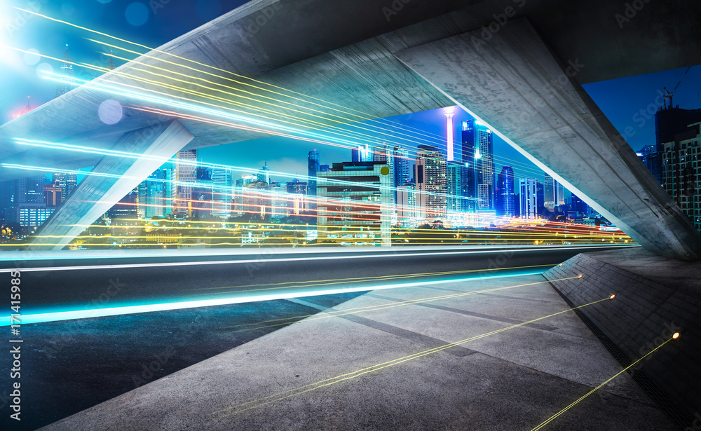 Empty asphalt road under the bridge during the night with light trails and beautiful city skyline background .