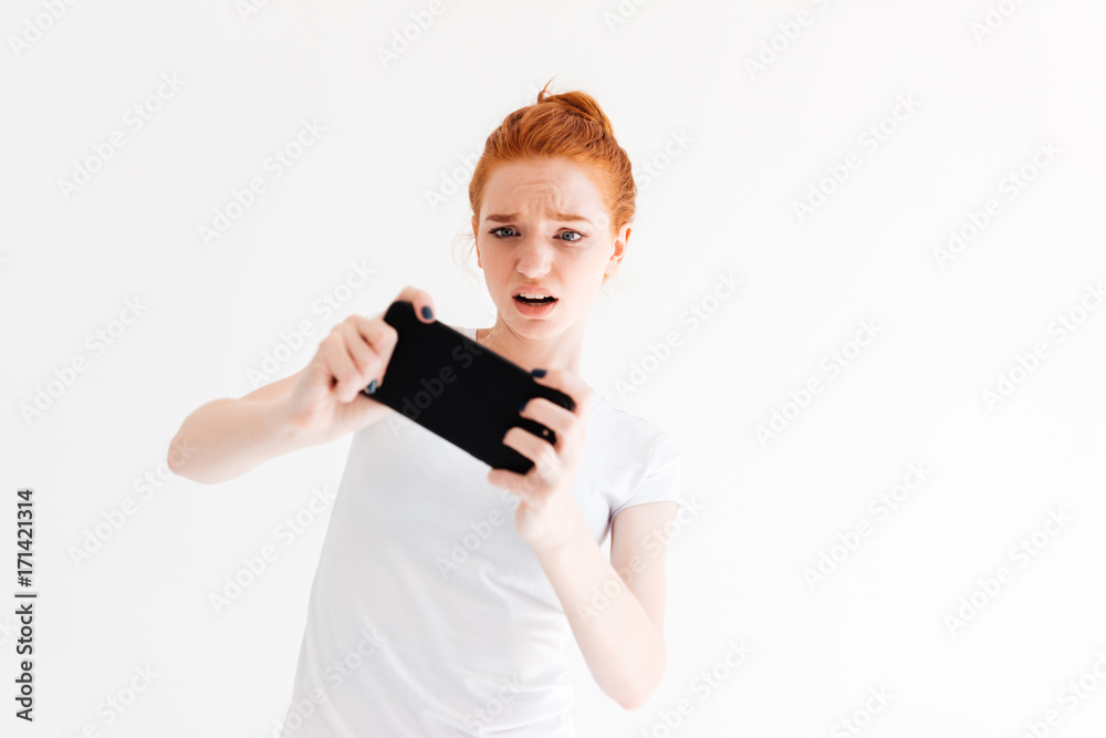 Upset ginger woman in t-shirt playing on her smartphone Upset ginger woman in t-shirt playing on her smartphone