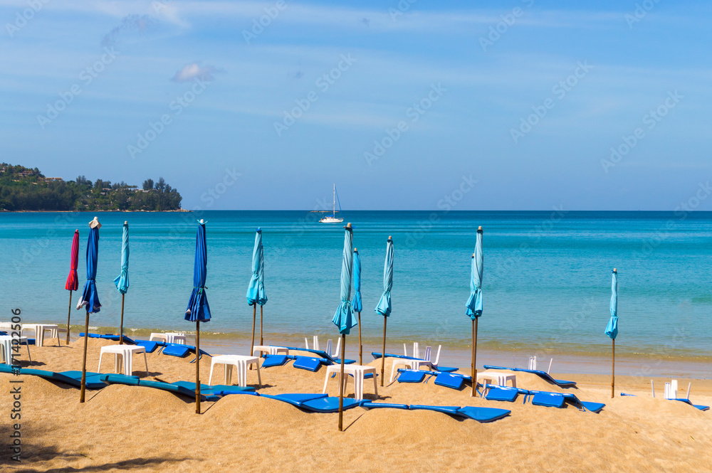 The low season at the seaside. Closed umbrellas on a beach with blue sea The low season at the seaside. Closed umbrellas on a beach with blue sea