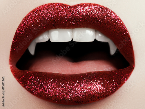 Fototapeta Female lips with glittering red lipstick, vampire teeth