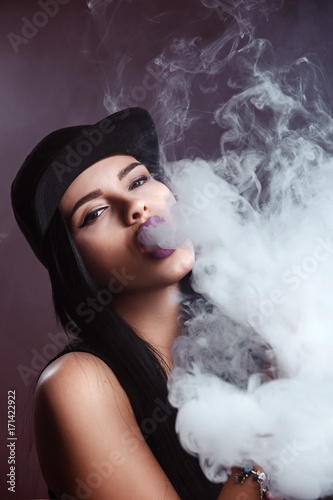 Young sexy woman is vaping. A cloud of vapor. Studio shooting.
