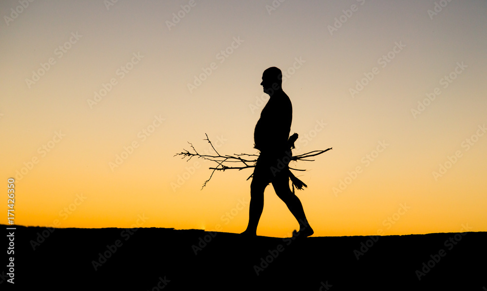Silhouette of a man with firewood at sunset