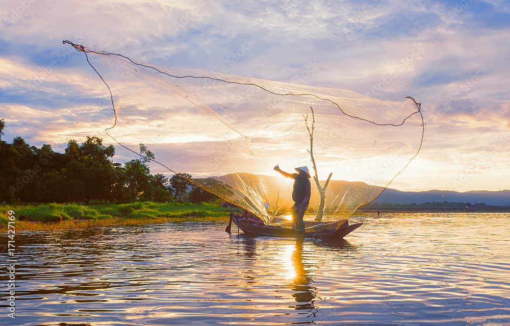 Fisherman on wooden boat casting a net for catching freshwater fish in  reservoir. Stock Photo