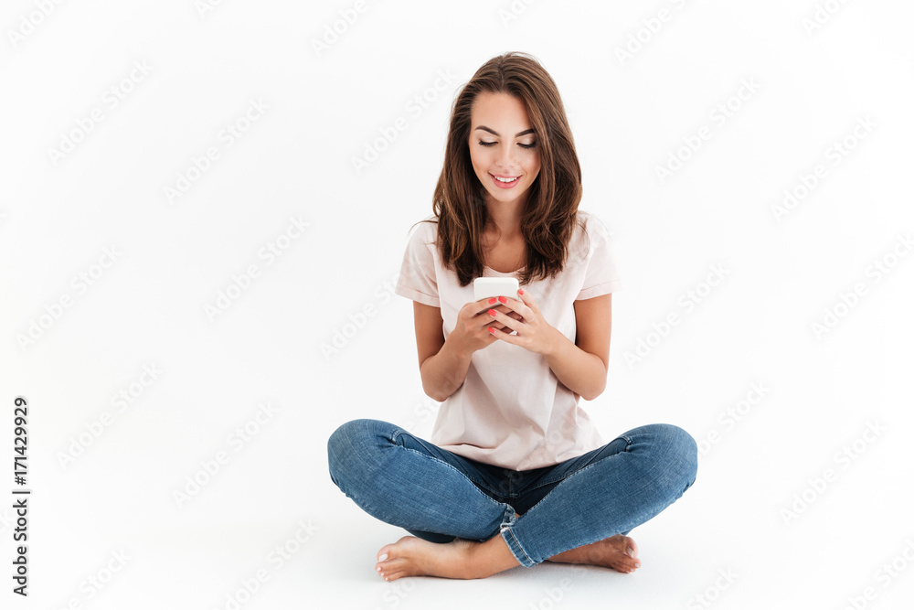 Smiling brunette woman sitting on the floor and using smartphone Smiling brunette woman sitting on the floor and using smartphone