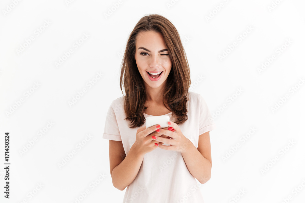 Happy brunette woman holding smartphone and winks at the camera Happy brunette woman holding smartphone and winks at the camera