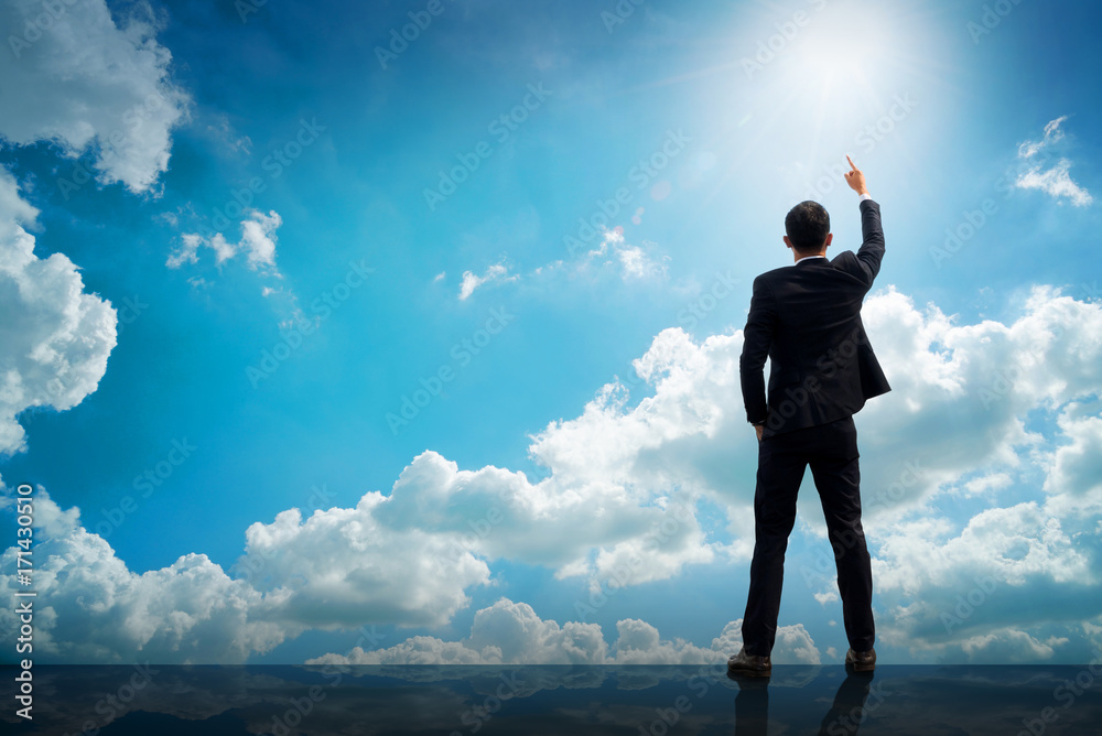 Back of successful businessman pointing up with his finger standing on top of building with sunlight sky background. Young man reaching goals, success and achievement concept. Copy space. Back of successful businessman pointing up with his finger standing on top of building with sunlight sky background. Young man reaching goals, success and achievement concept. Copy space.
