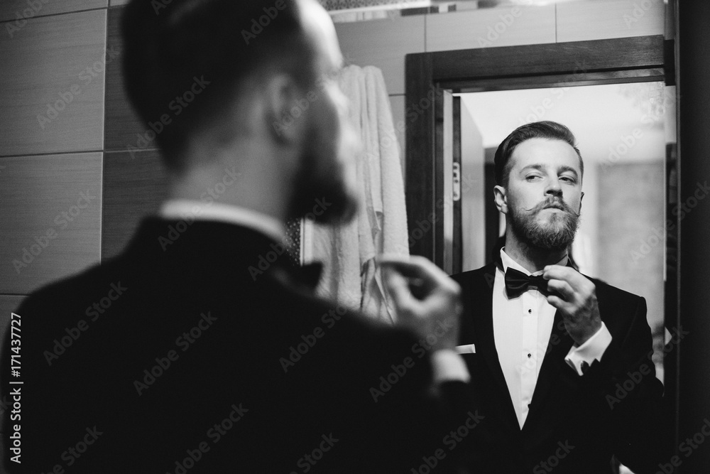 Handsome stylish groom with beard and mustache getting dressed and preparing for the wedding day.