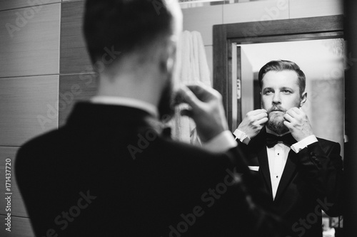 Handsome stylish groom with beard and mustache getting dressed and preparing for the wedding day.