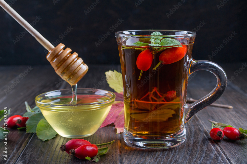Rose hip tea in transparent cup with honey and fresh berries. Vitamin C drink on dark background. Rose hip tea in transparent cup with honey and fresh berries. Vitamin C drink on dark background.