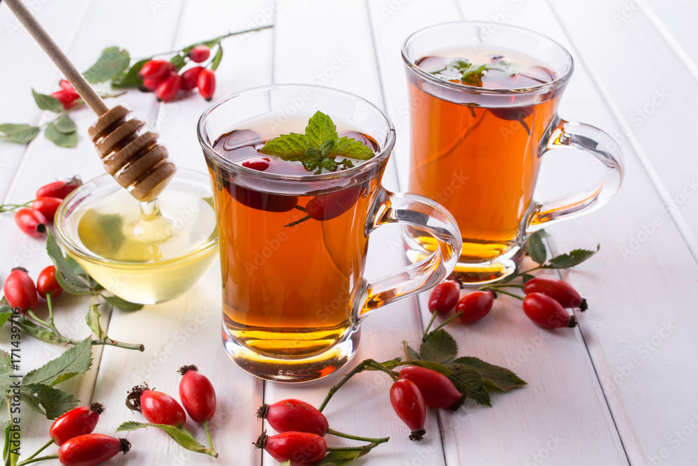 Rose hip tea in transparent cup with honey and fresh berries. Vitamin C drink on white background. Rose hip tea in transparent cup with honey and fresh berries. Vitamin C drink on white background.