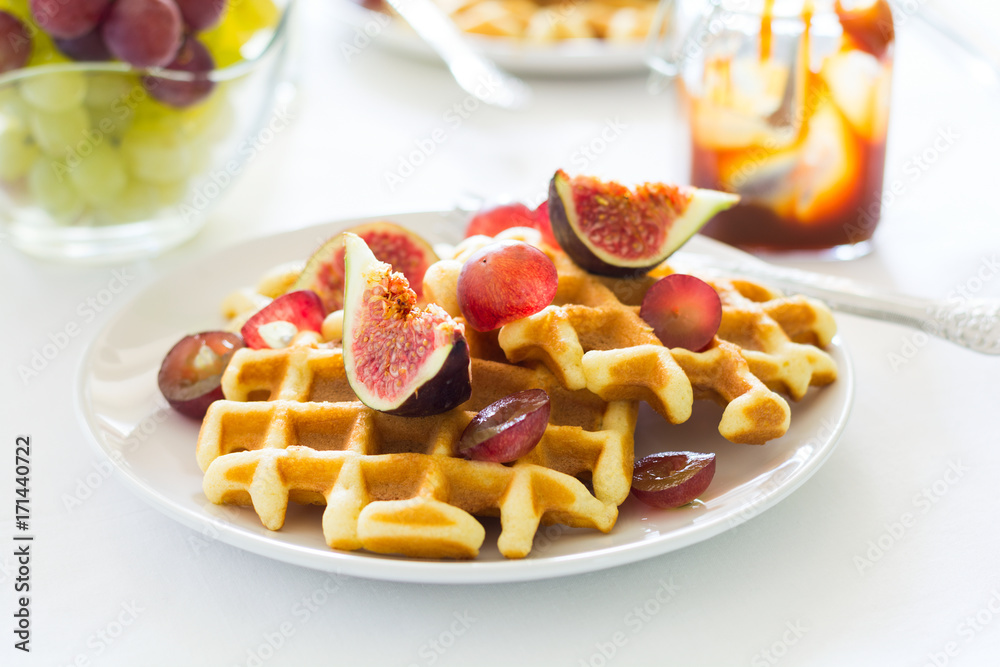 Healthy breakfast: Belgian waffles with figs, grapes and caramel on white table cloth. Selective focus Healthy breakfast: Belgian waffles with figs, grapes and caramel on white table cloth. Selective focus