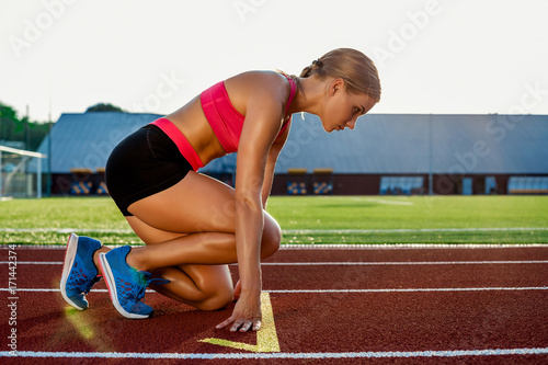 Young woman athlete at starting position ready to start a race on racetrack.