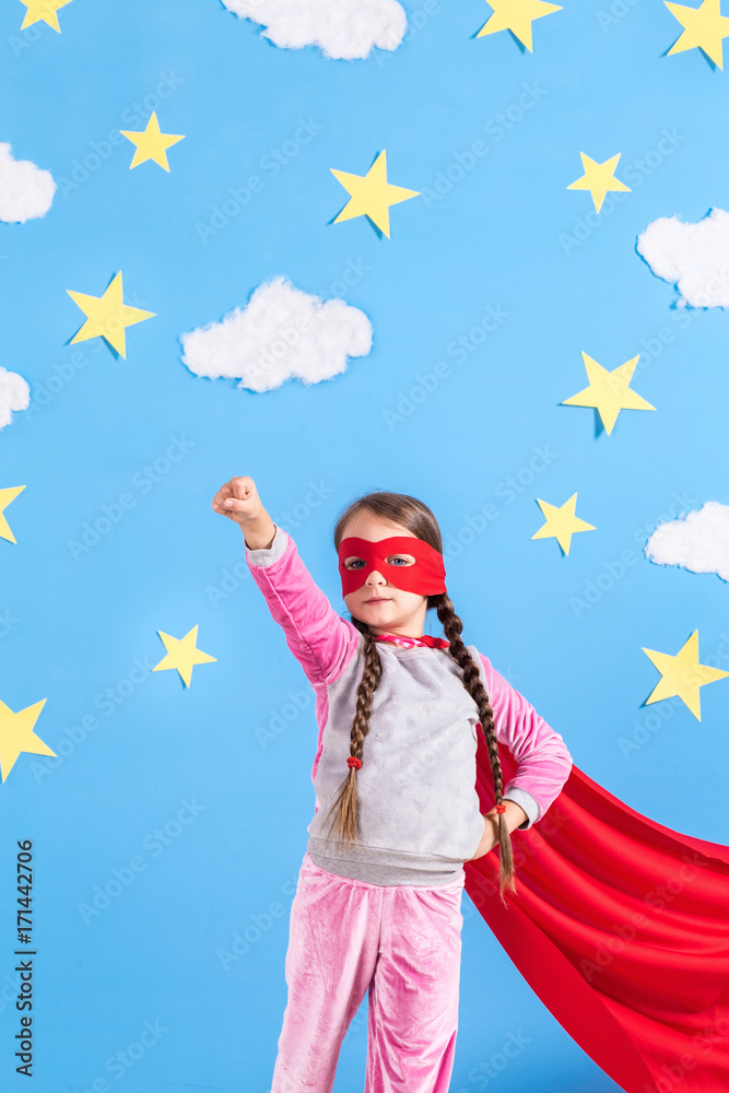 Little child plays superhero. Kid on the background of bright blue wall.