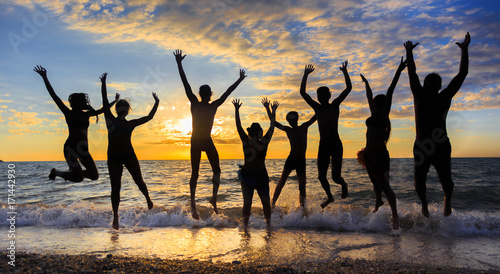 Silhouettes of happy jumping people at sea surf