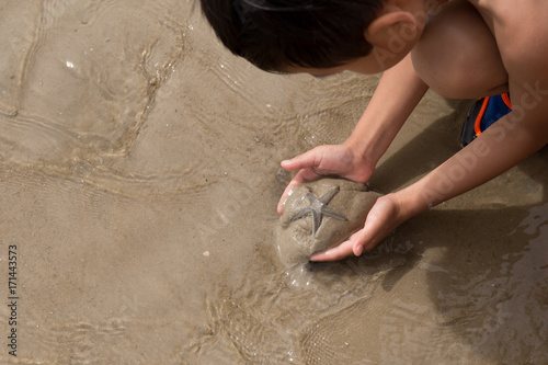 Little boy holding starfish on beach photo