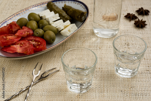 Two glasses and bottle of traditional drink Ouzo or Raki and appetizers on natural matting