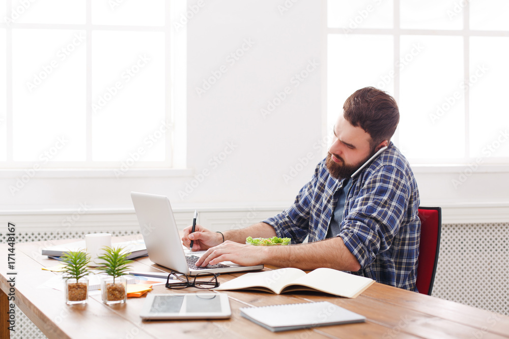 Young busy businessman with laptop has lunch in modern white office