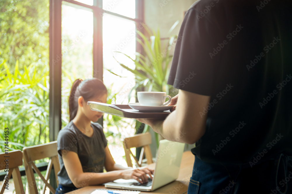 Woman working on laptop computer with waiter serving a cup of coffee